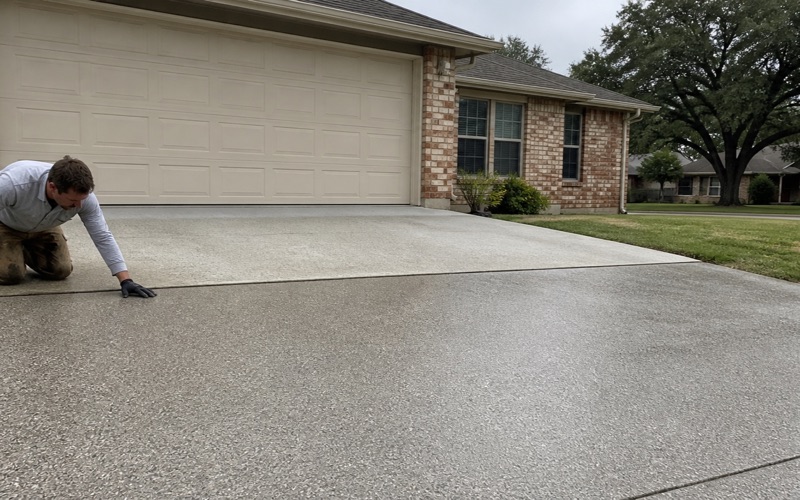A Pflugerville concrete driveway half coated, with the expansion joint at the property line left open where new work meets old.